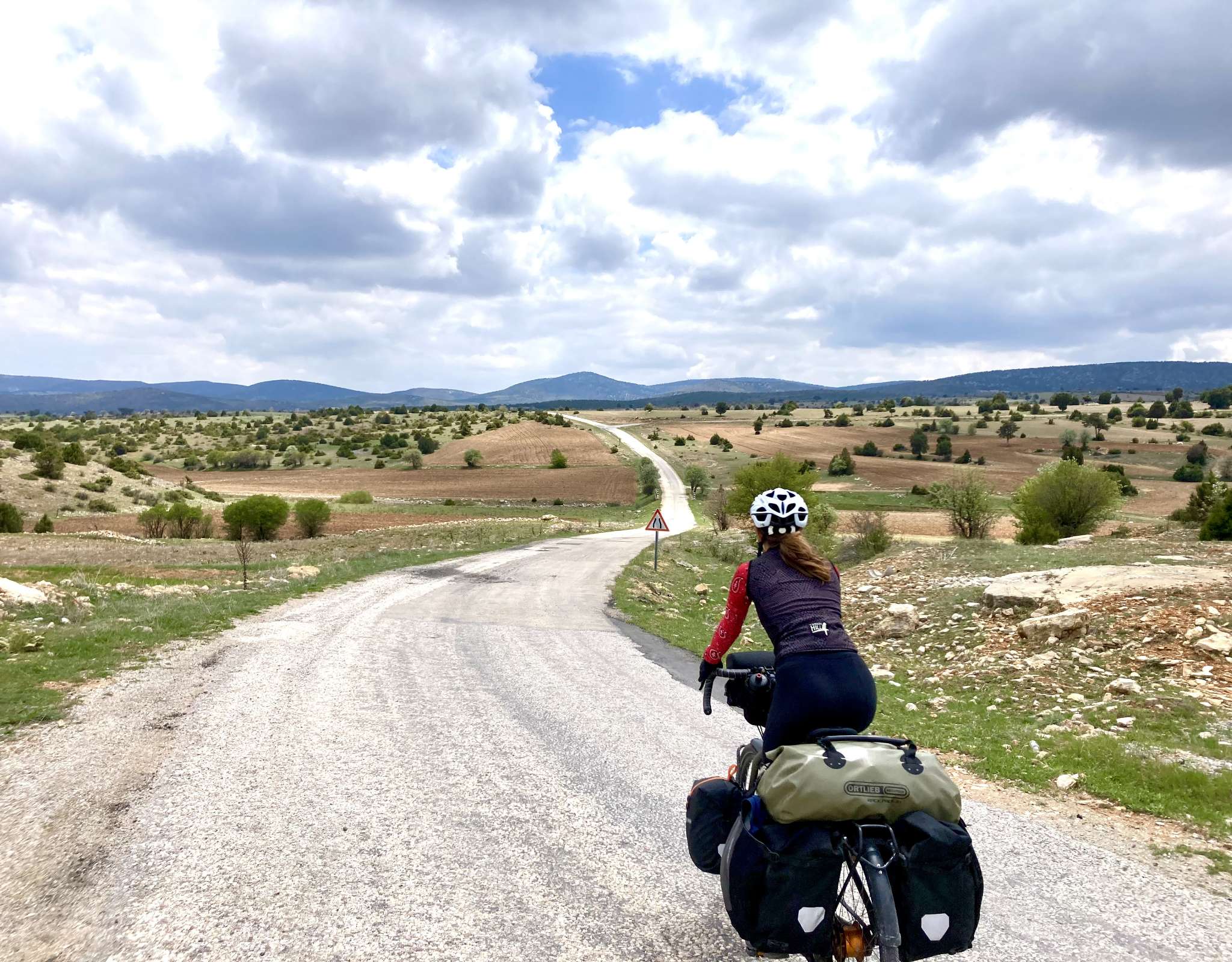 Marie met volle bepakking kijkt uit over een kronkelende weg door een heuvelachtig landschap.